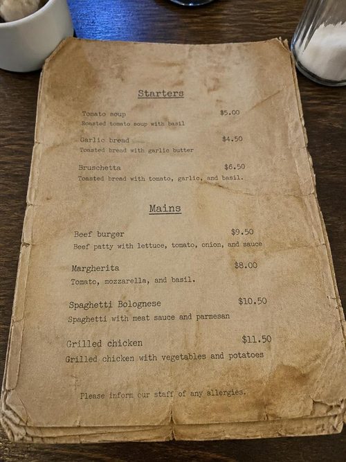 A tatty old paper restaurant menu photographed on a cafe table